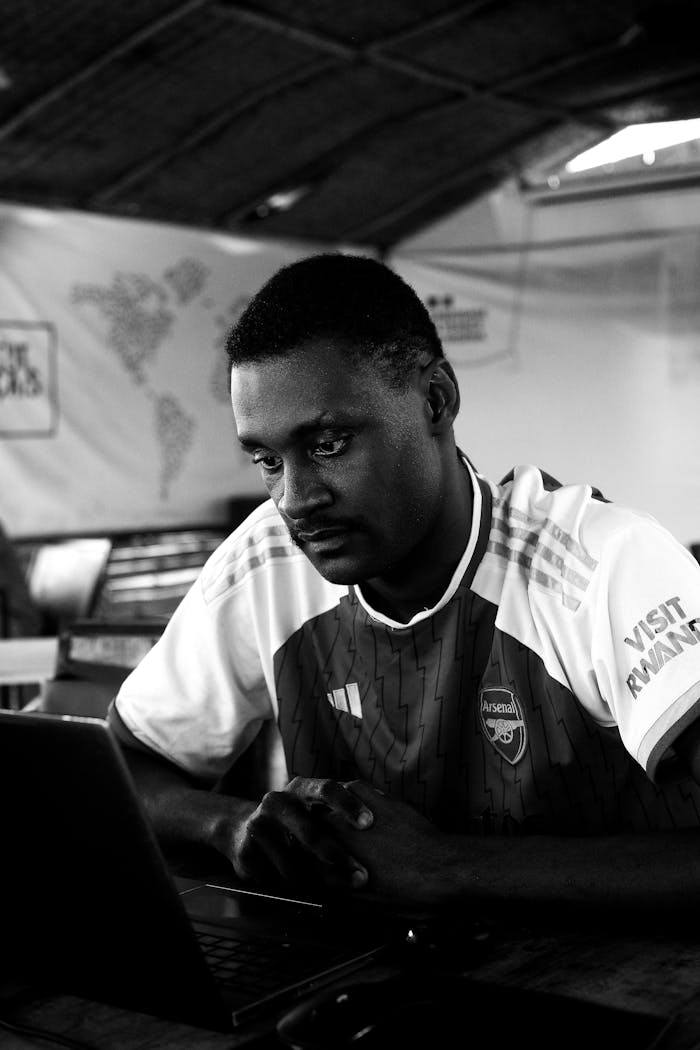 Monochrome photo of a man focused on a laptop in a casual indoor setting.